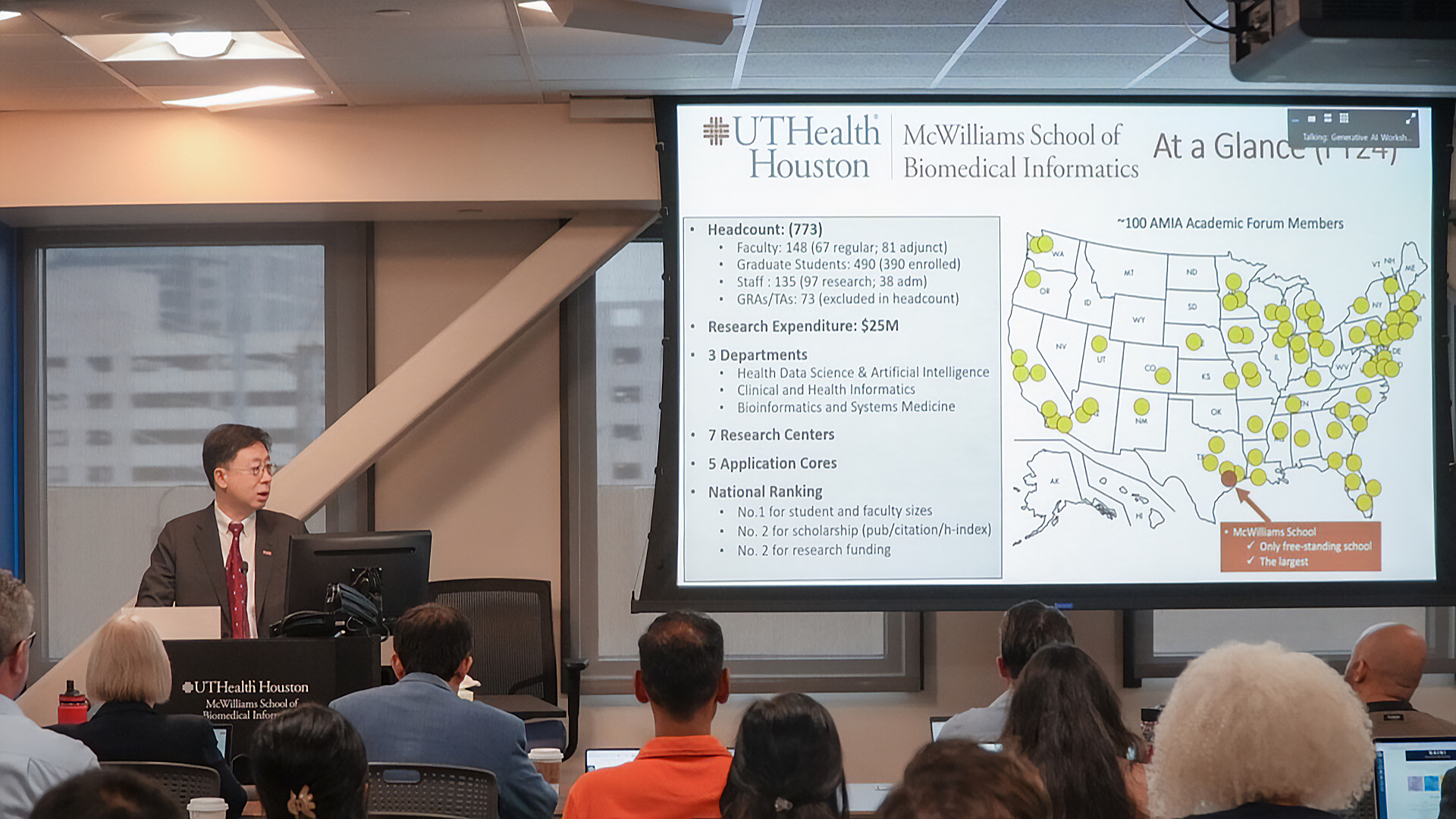 Speaker presenting UTHealth Houston McWilliams School of Biomedical Informatics overview to an audience with a projected slide showing stats and a U.S. map. 