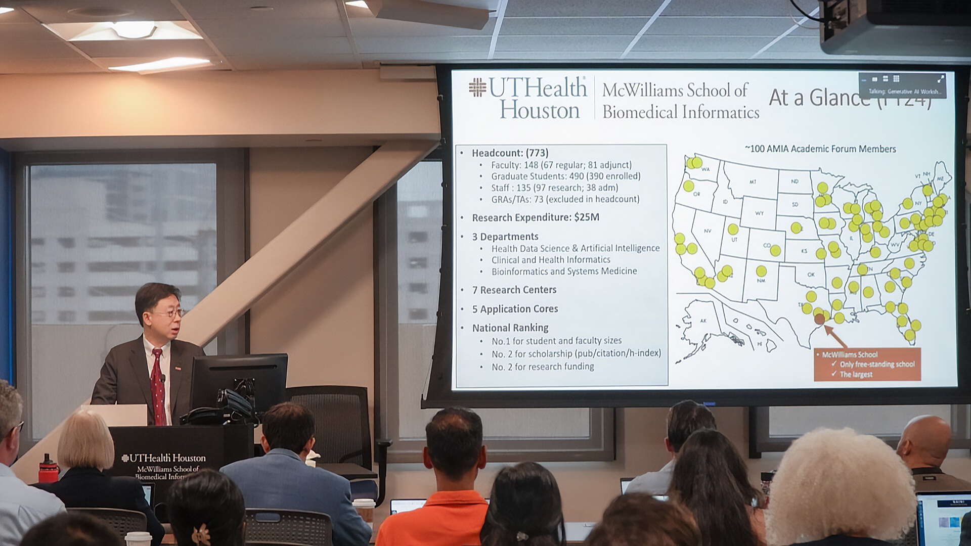 Speaker presenting UTHealth Houston McWilliams School of Biomedical Informatics overview to an audience with a projected slide showing stats and a U.S. map.